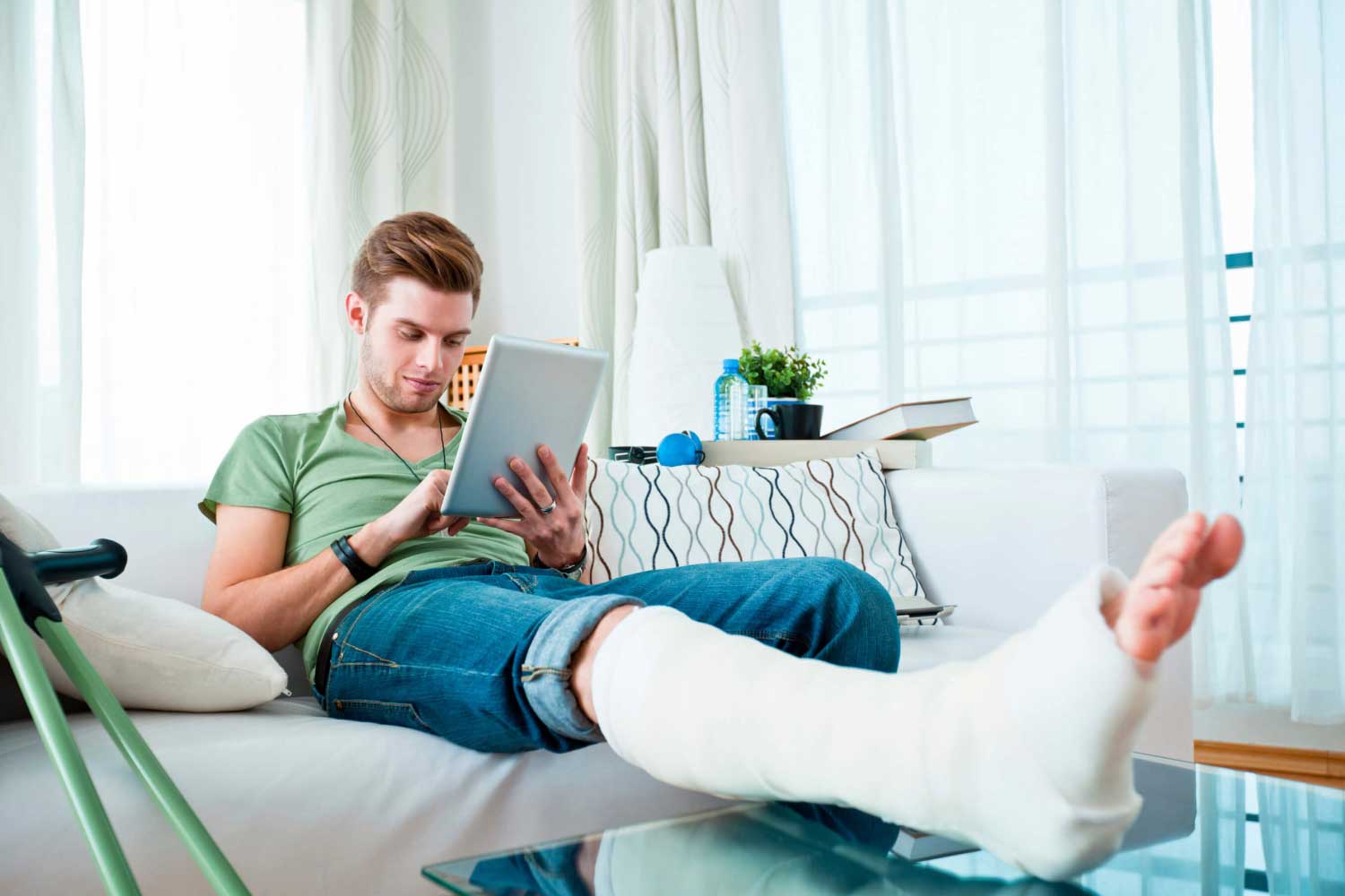 young man working on mobile device with his broken leg in a plaster cast